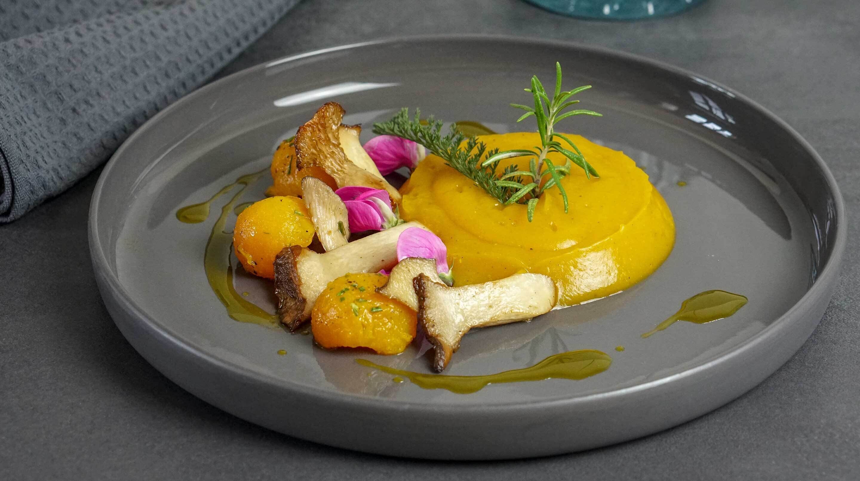 Un piatto con salsa gialla, funghi e un rametto di rosmarino.