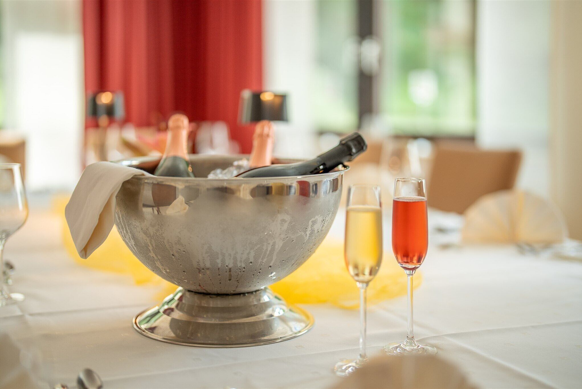 A silver ice bucket with a bottle and a wine glass on a table.