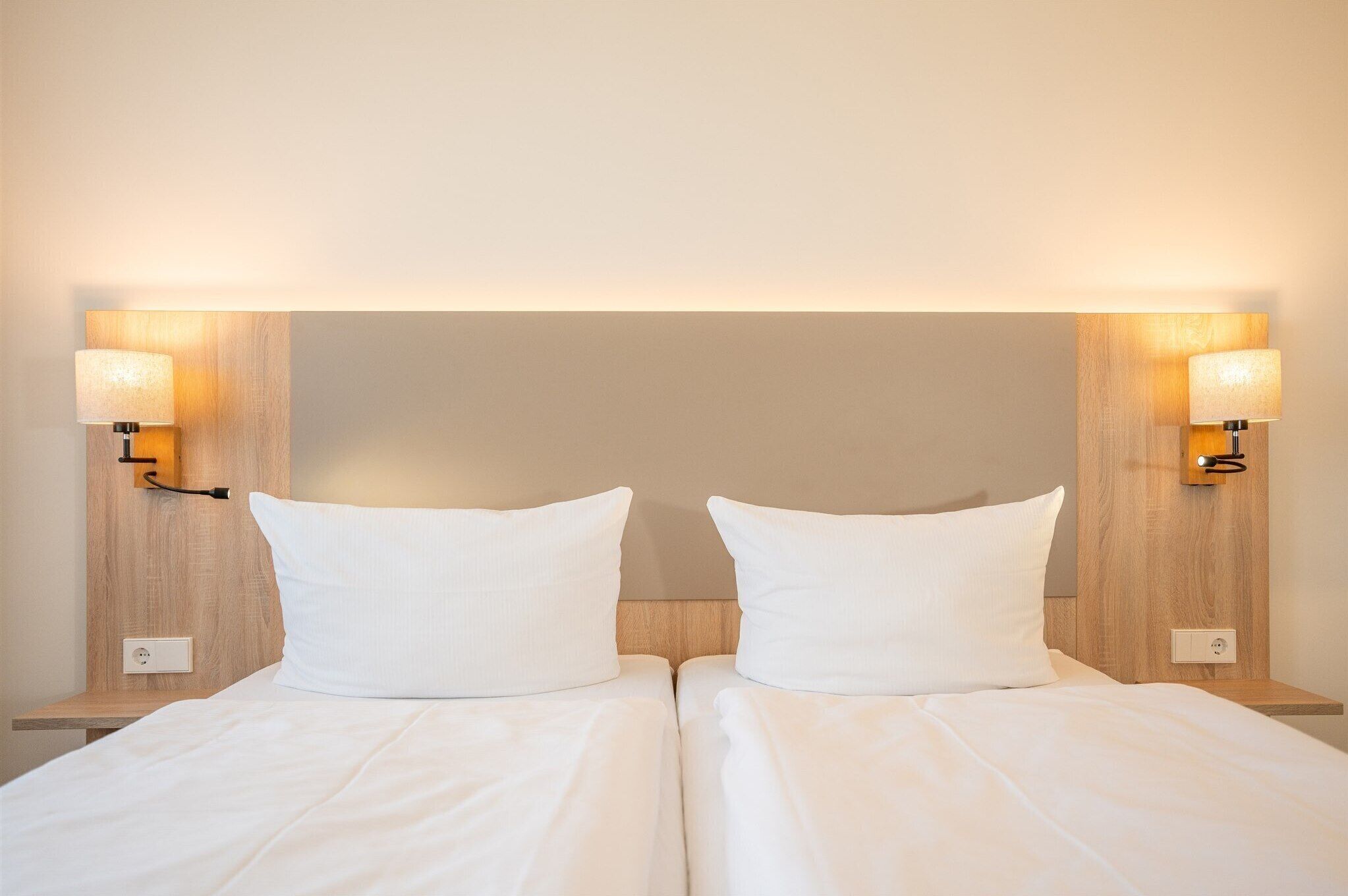 A double bed with white linens, two bedside lamps, and a wooden headboard.