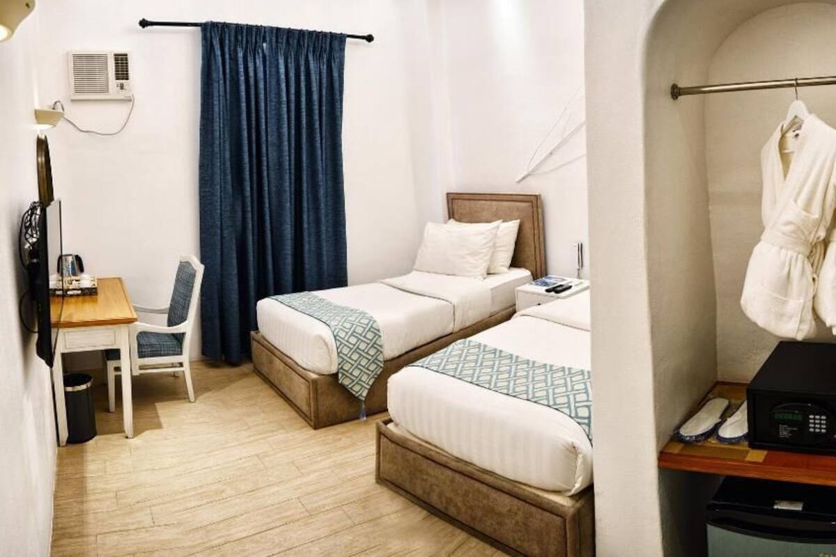 Habitación de hotel con dos camas, un escritorio con silla, una mesita pequeña, microondas y perchero.
