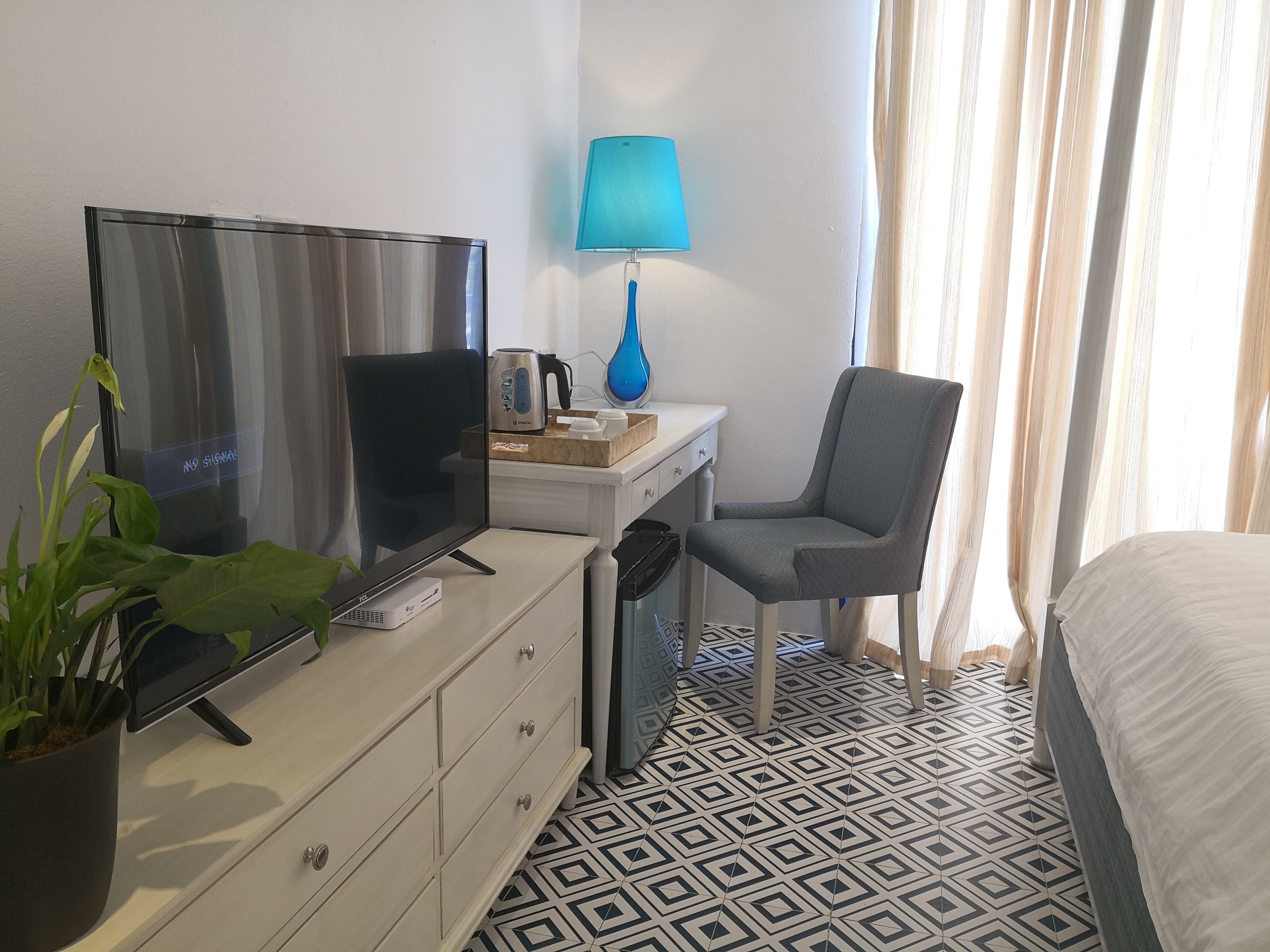 Et hotelværelse med fjernsyn, skrivebord med lampe, stol, seng og et gulv med et mønster.