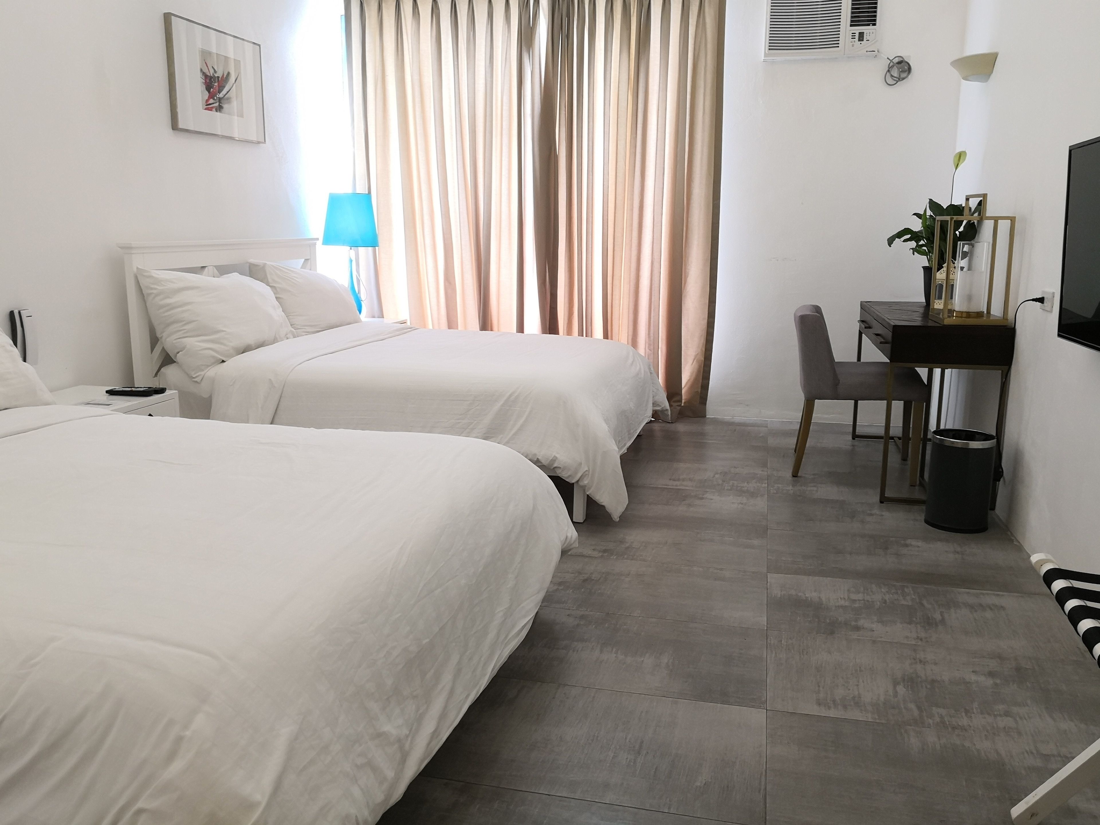 Une chambre d’hôtel avec deux lits, un bureau avec une chaise, une télévision, une lampe et une poubelle.