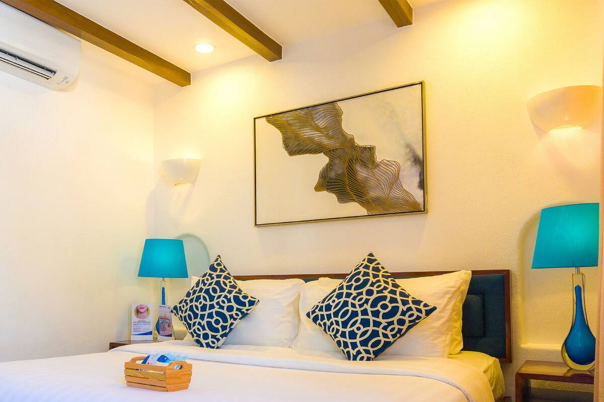 Habitación de hotel con cama, dos lámparas de pared, una obra de arte abstracta enmarcada y una mesita de noche con lámpara.