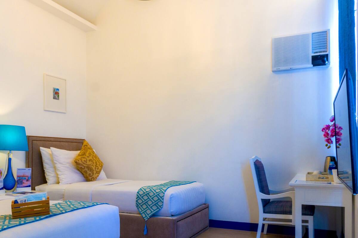 Habitación de hotel con dos camas, un escritorio, una silla, una lámpara y un cuadro en la pared.