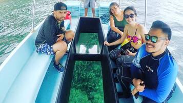A boat with four people seated, a person standing at the back, and a clear view of the water through a window.