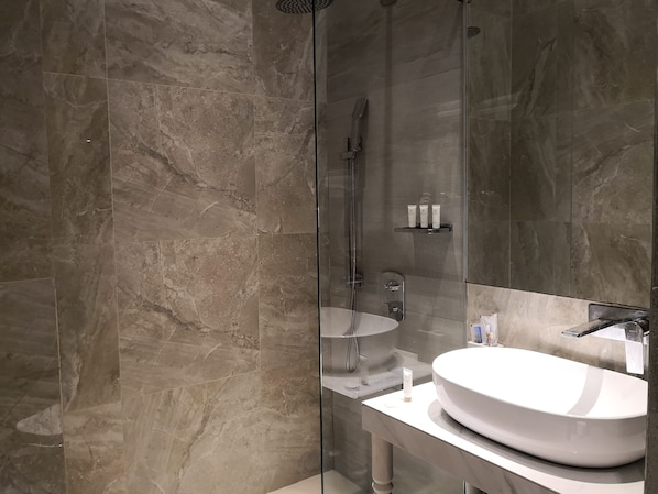 A modern bathroom with a glass-enclosed shower, a white sink, and a marble-tiled wall. - Camp Netanya Resort & Spa (Mabini)