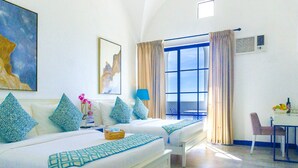 Una habitación de hotel con cama, escritorio con silla, ventana con cortinas y obras de arte en las paredes.