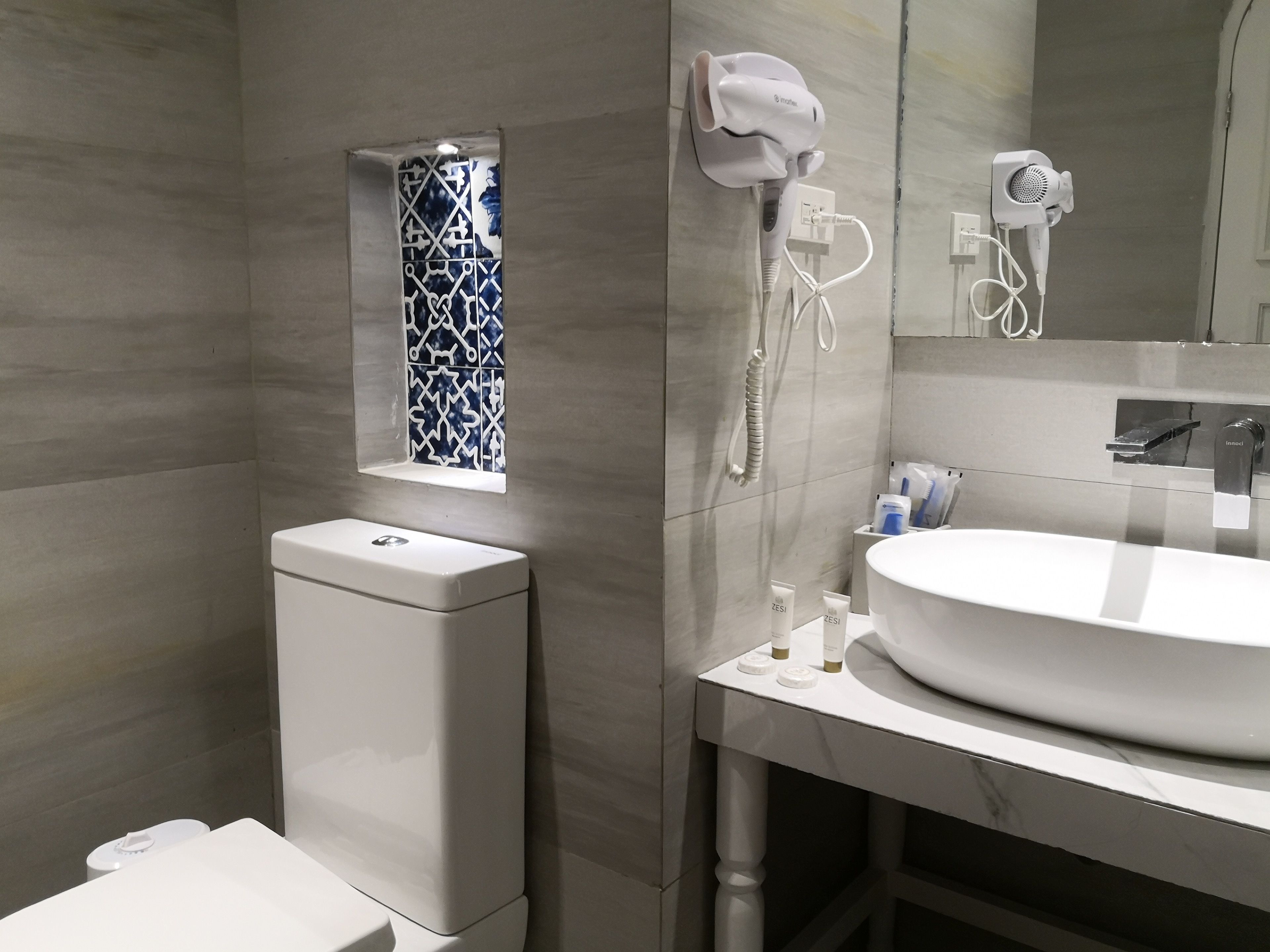 Un baño moderno con inodoro, bidé y lavamanos con espejo. Hay dos secadores de pelo fijados a la pared.