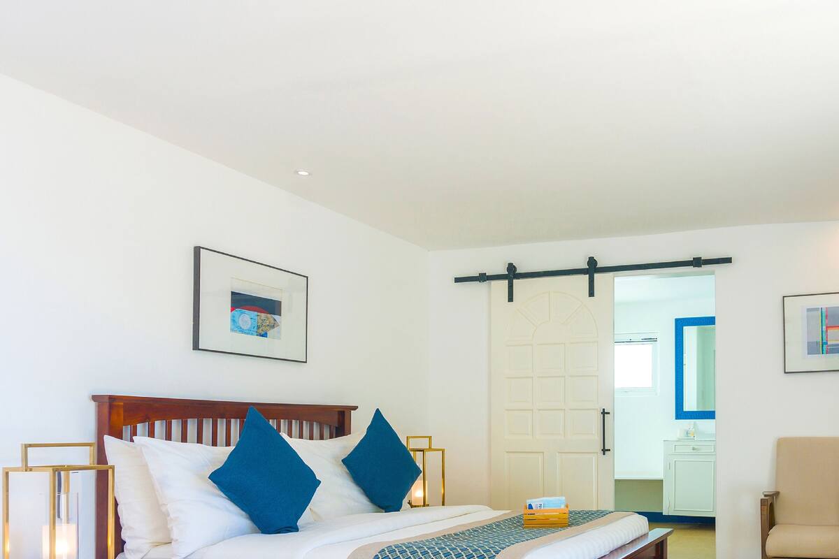 Habitación de hotel con una cama, una silla, una mesita con un frutero y un espejo en la pared.