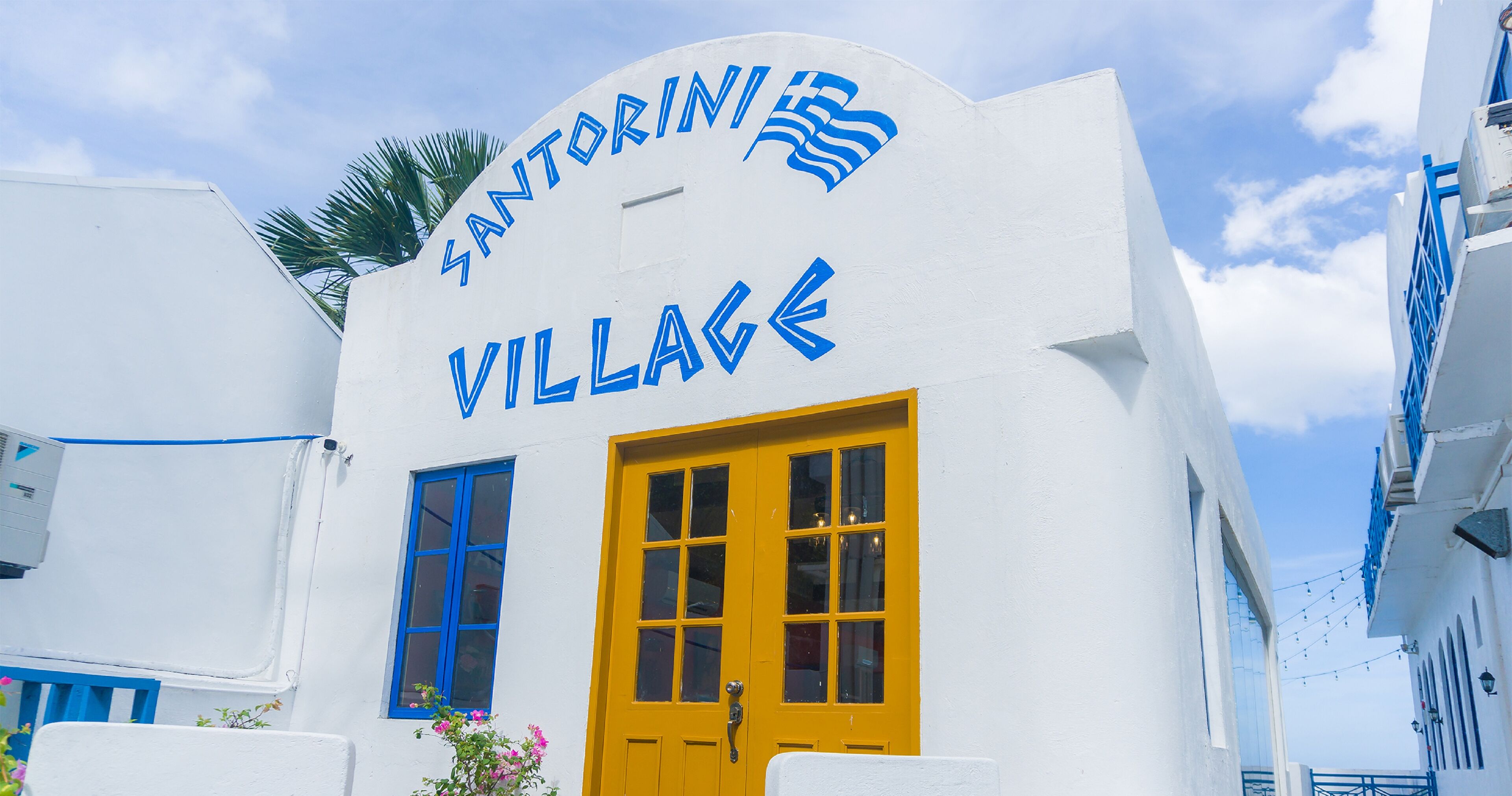 A building with a white facade and a yellow door, labeled "Santorini Village".