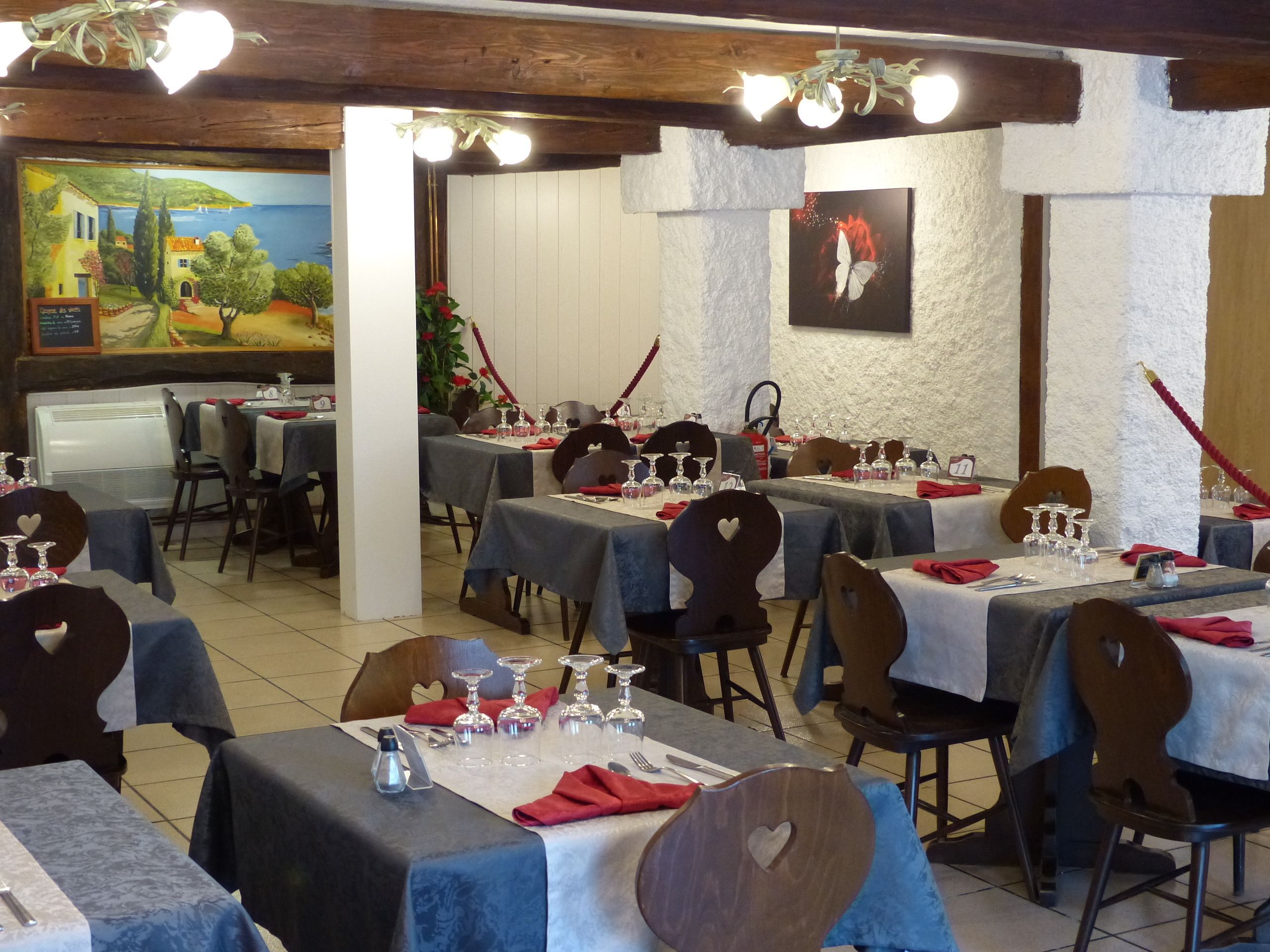 Un restaurante con varias mesas dispuestas para comer, cada una con mantel blanco y servilletas rojas.