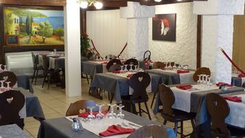 Un restaurante con varias mesas dispuestas para comer, cada una con mantel blanco y servilletas rojas.