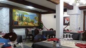 A restaurant interior with tables set for dining, a large mural on the wall, and a chandelier. - Hotel restaurant la vieille ferme (Etupes)