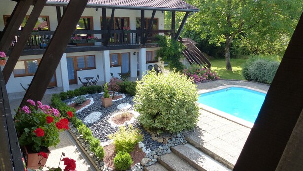 A poolside area with a wooden pergola, a swimming pool, and a garden with various plants and flowers. - Hotel restaurant la vieille ferme (Etupes)