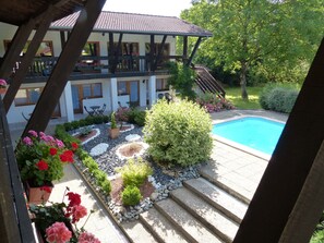 Uma área à beira da piscina com um pérgola de madeira, uma piscina e um jardim com diversas plantas e flores.