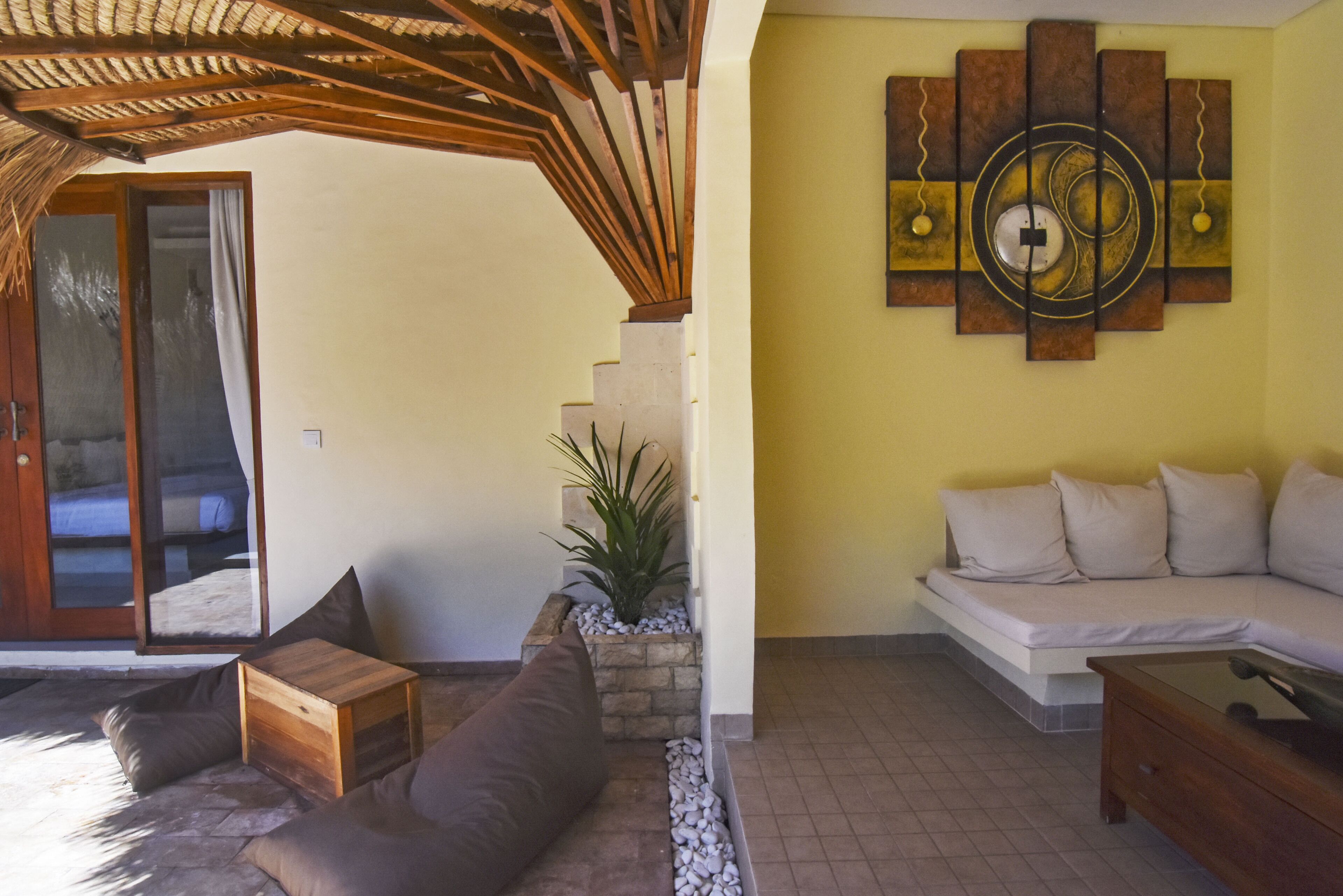A living room with a sofa, a wooden coffee table, a stone planter with a plant, and a wall art piece.