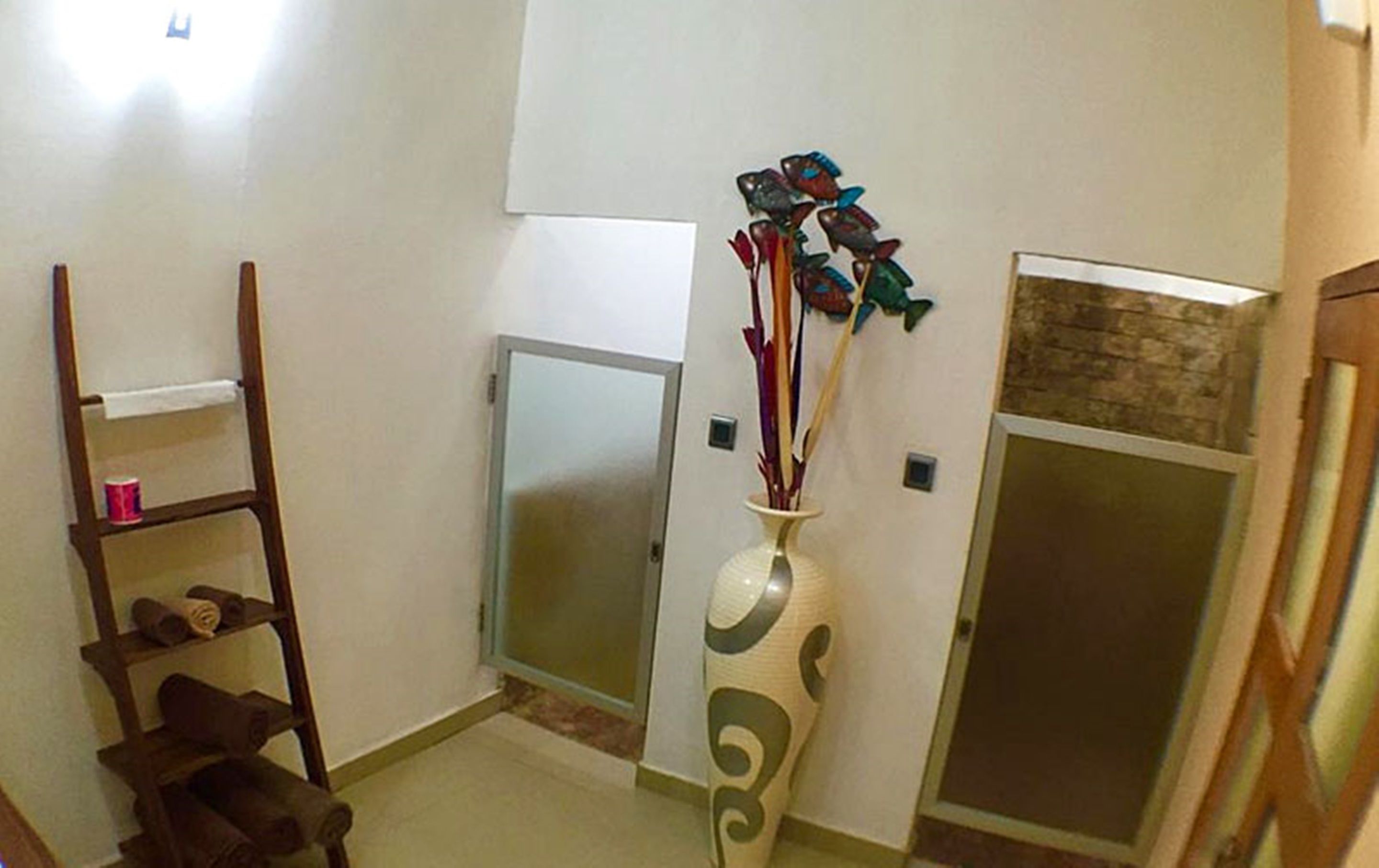 Una habitación con una escalera de madera, un florero blanco con detalles decorativos y una puerta con un panel de vidrio.