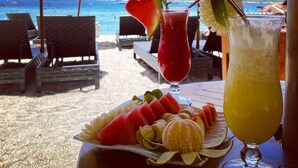 A beachside table with a fruit platter, two drinks, and umbrellas labeled "la bella". - La Bella - Hotel Villa & Spa (Gili Trawangan)