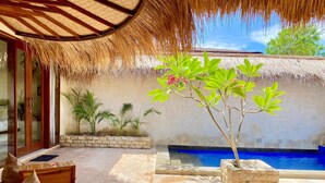 A poolside area with a thatched roof, a stone planter with a tree, and a tiled floor. - La Bella - Hotel Villa & Spa (Gili Trawangan)