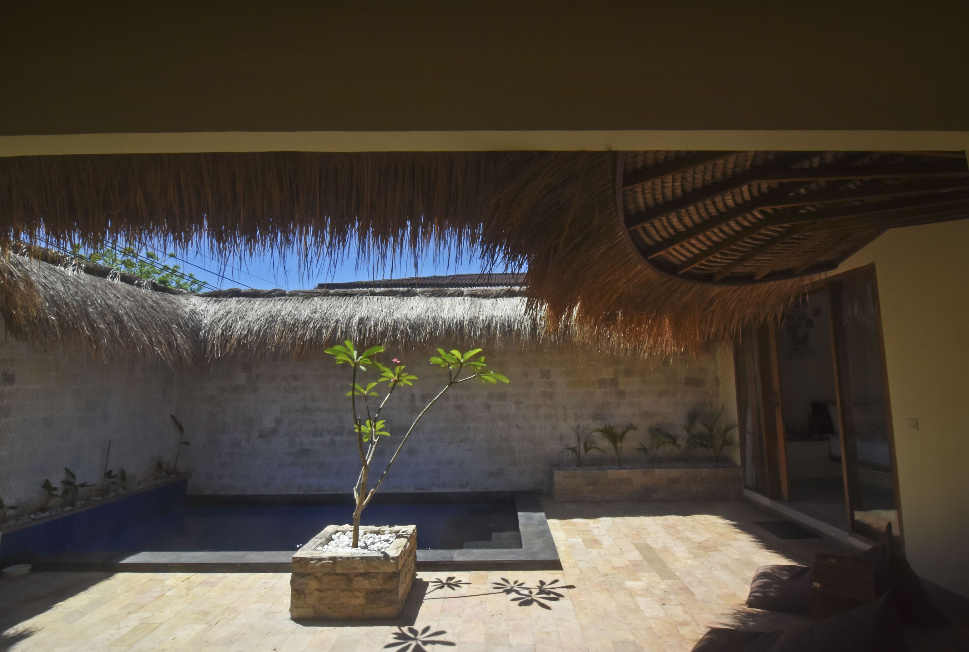 Una habitación con techo de paja, una pequeña planta en maceta, un banco de piedra y vistas al cielo.