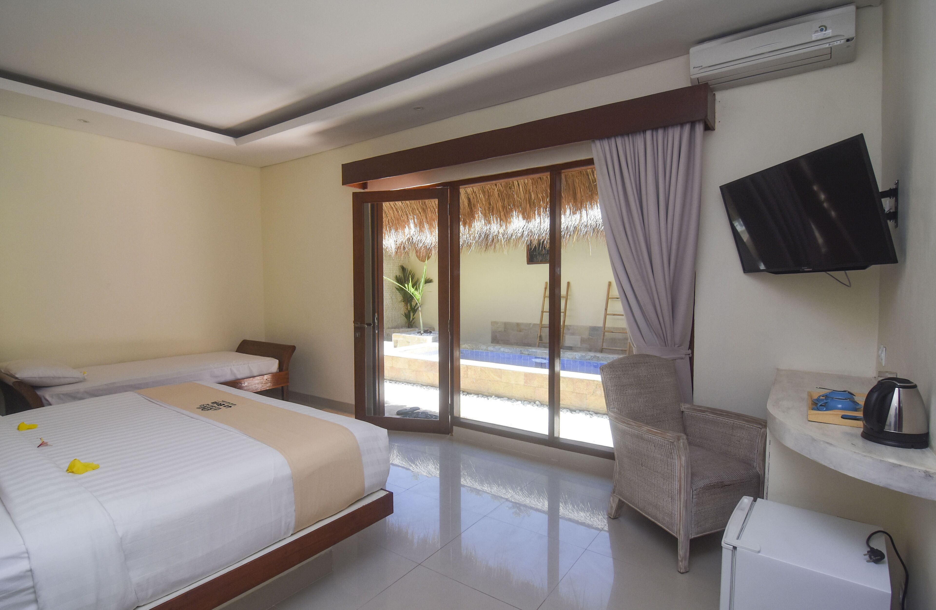 A hotel room with two beds, a TV, a small table with a kettle, and a chair.