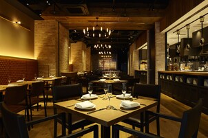 A restaurant with multiple tables set for dining, featuring a brick wall and wooden ceiling.