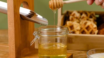 A honey dipper dripping honey into a glass jar, with waffles in the background.