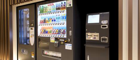A vending machine with a variety of drinks and snacks, a money exchange machine, and a coin outlet.