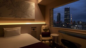 Une chambre d’hôtel avec un lit, une chaise, une petite table et une vue sur le paysage urbain de nuit.
