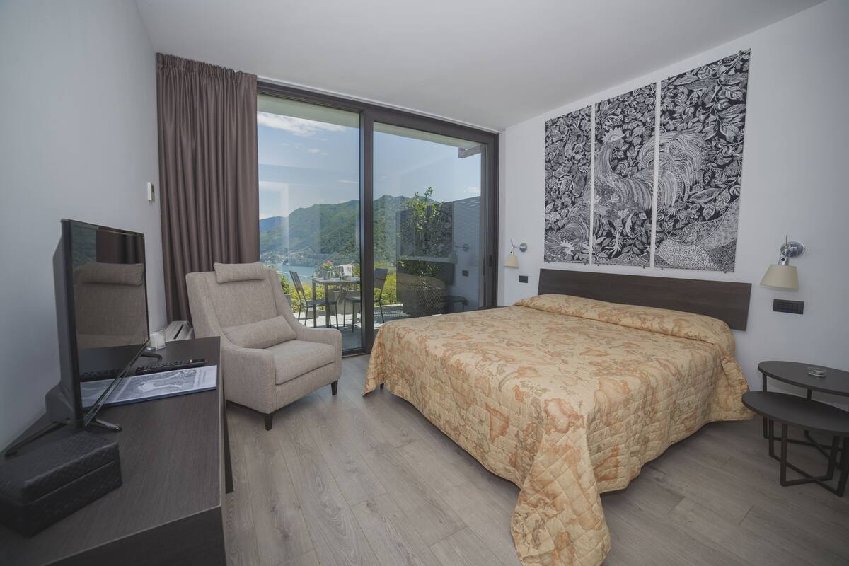 A modern hotel room with a large bed, a desk with a computer, a chair, and a view of the outdoors.