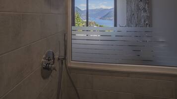 A modern bathroom with a shower, a view of mountains and a lake, and a large window.