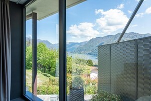 Habitación con un ventanal que ofrece vistas a montañas, un lago y un pueblo lejano.