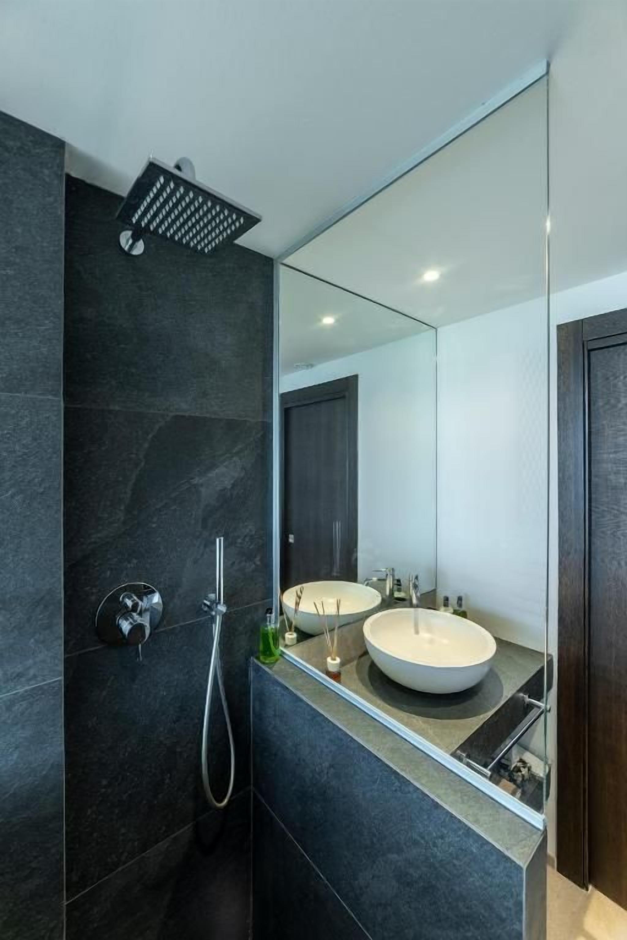 A modern bathroom with a large mirror, two sinks, and a shower.
