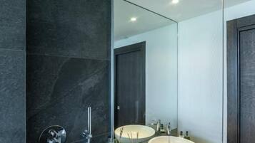 A modern bathroom with a large mirror, two sinks, and a shower.
