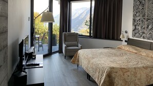 A hotel room with a bed, a desk with a computer, a chair, and a large window offering a mountain view. - B&B Vista Lago (Como)