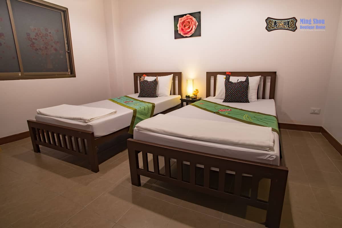 A hotel room with two single beds, a nightstand, a lamp, and a window with a view of a tree.