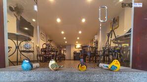 A reception area with a staircase, a dining area in the background, and decorative bird figurines on the steps. - Ming Shou Boutique House (Phuket)