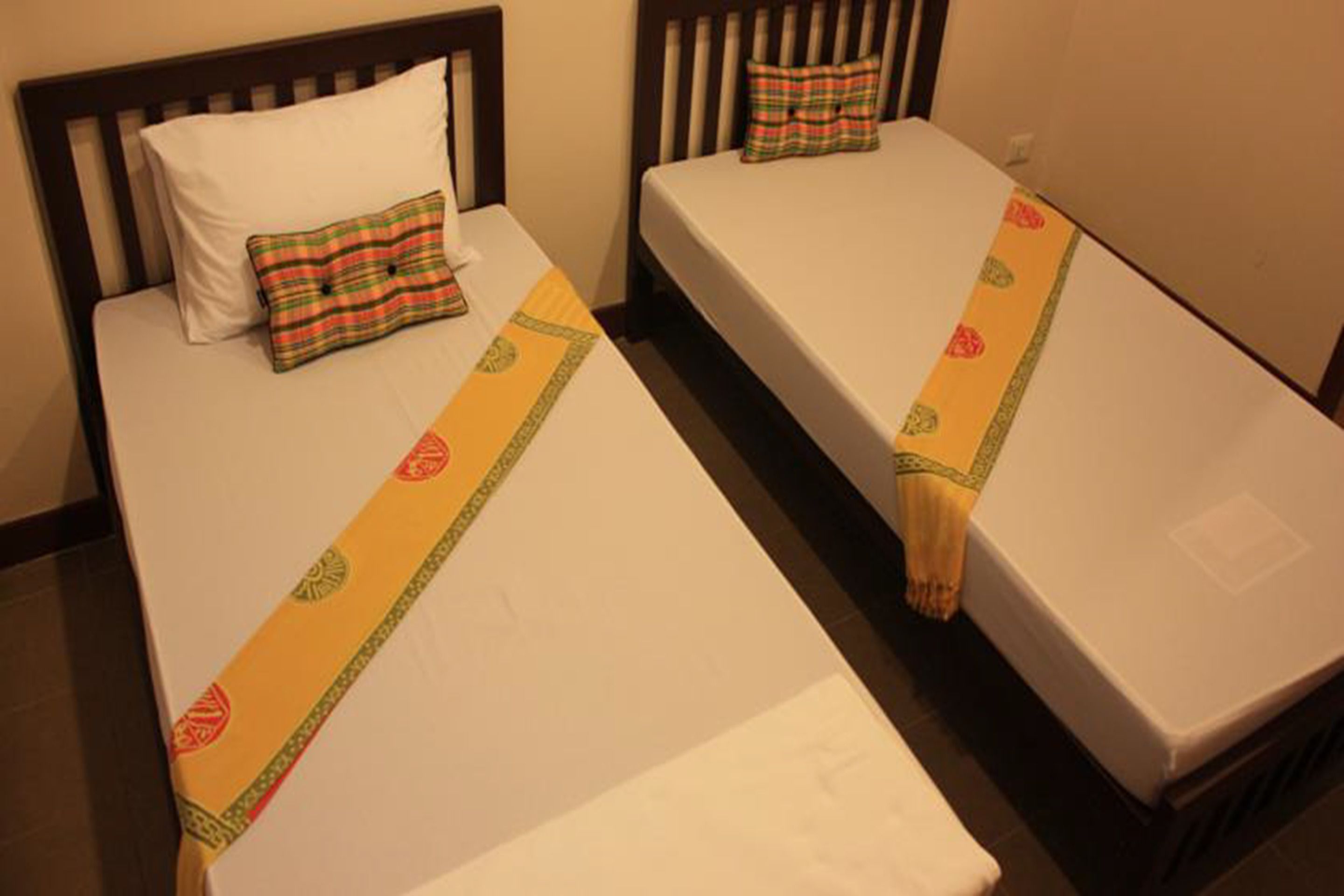 Dos camas individuales con sábanas blancas y un corredor decorativo amarillo. Cada cama tiene un almohadón y una funda a juego.