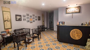 A room with a patterned floor, wooden furniture, a reception desk, and various framed pictures on the walls. - Ming Shou Boutique House (Phuket)