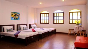 A hotel room with three single beds, a small table with a chair, and two arched windows with warm lighting. - Ming Shou Boutique House (Phuket)