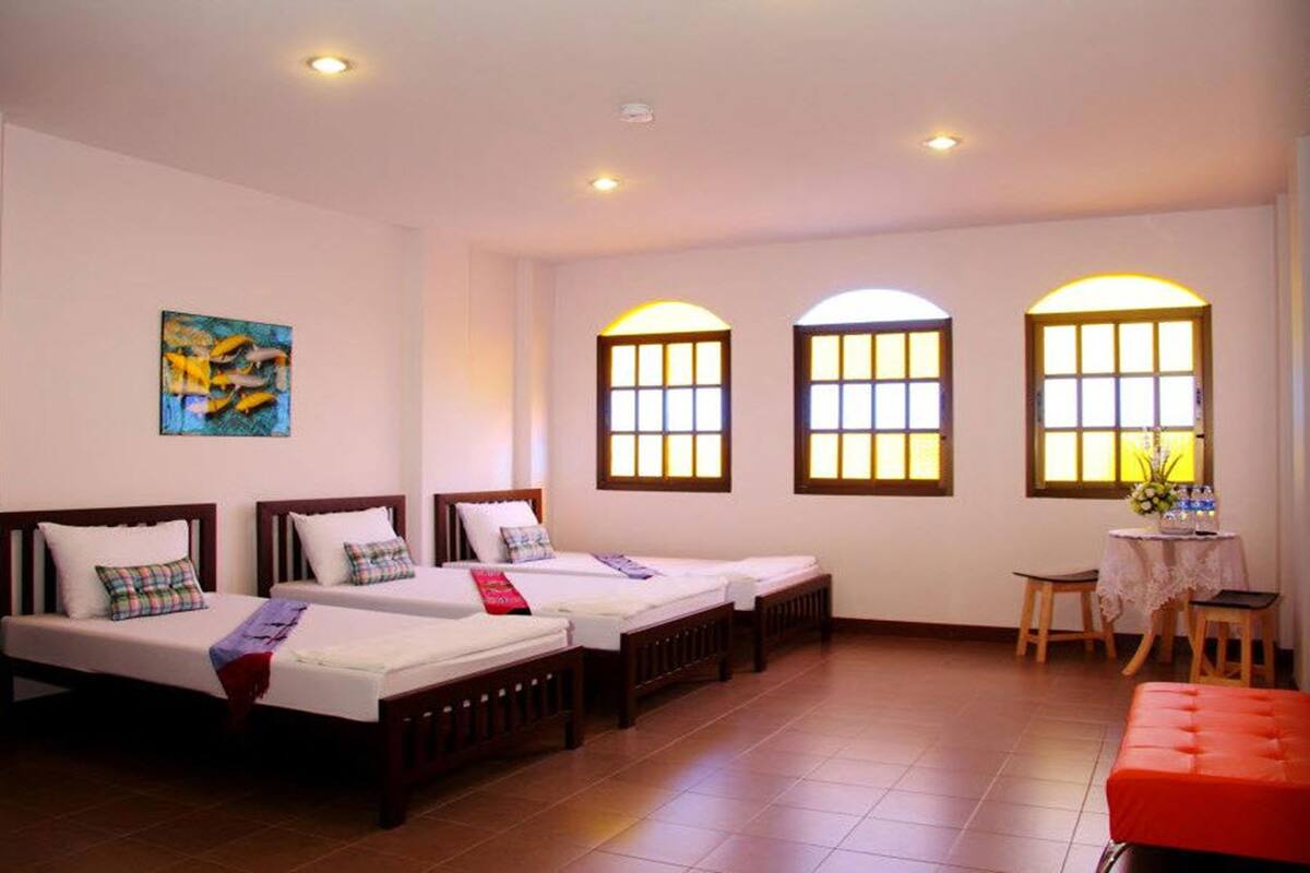 A hotel room with three single beds, a small table with a chair, and two arched windows with warm lighting.