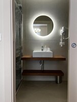 Une salle de bain moderne avec un miroir rond, un lavabo blanc et une douche.