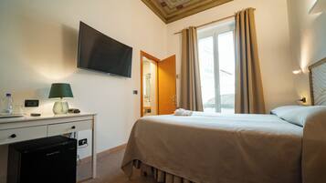 Habitación de hotel con cama, escritorio con lámpara, televisor y vistas al exterior.
