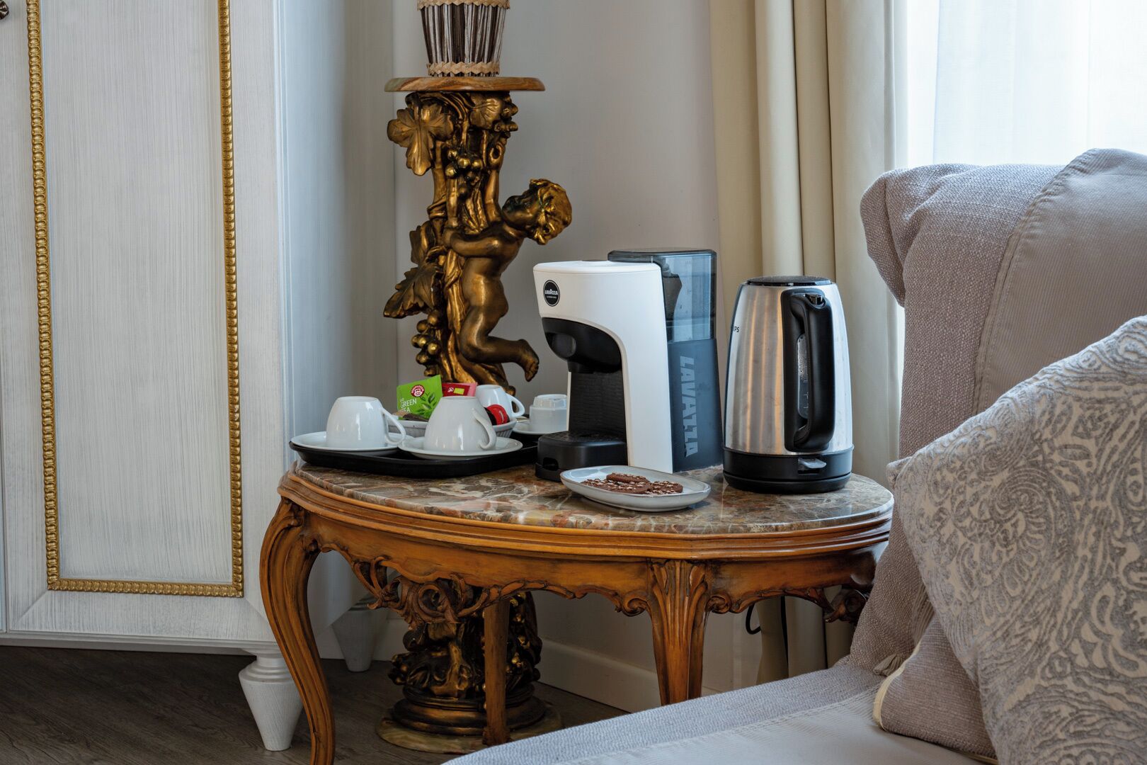 A room with a coffee maker, a plate of food, a cup, and a decorative golden statue on a table.