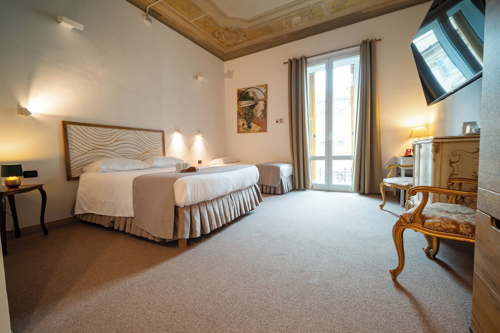 A hotel room with two beds, a desk, a chair, a TV, and a large window with curtains.