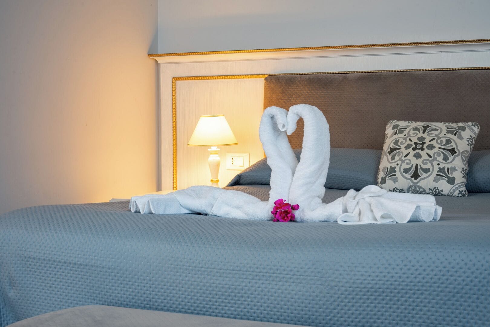 A hotel room with a bed, pillows, a lamp, and a decorative towel arrangement.
