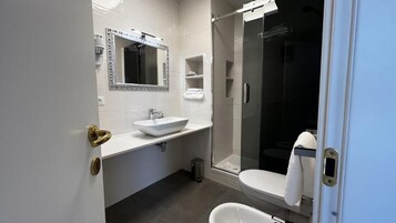 A modern bathroom with a white sink, a large mirror, a glass-enclosed shower, and a toilet.
