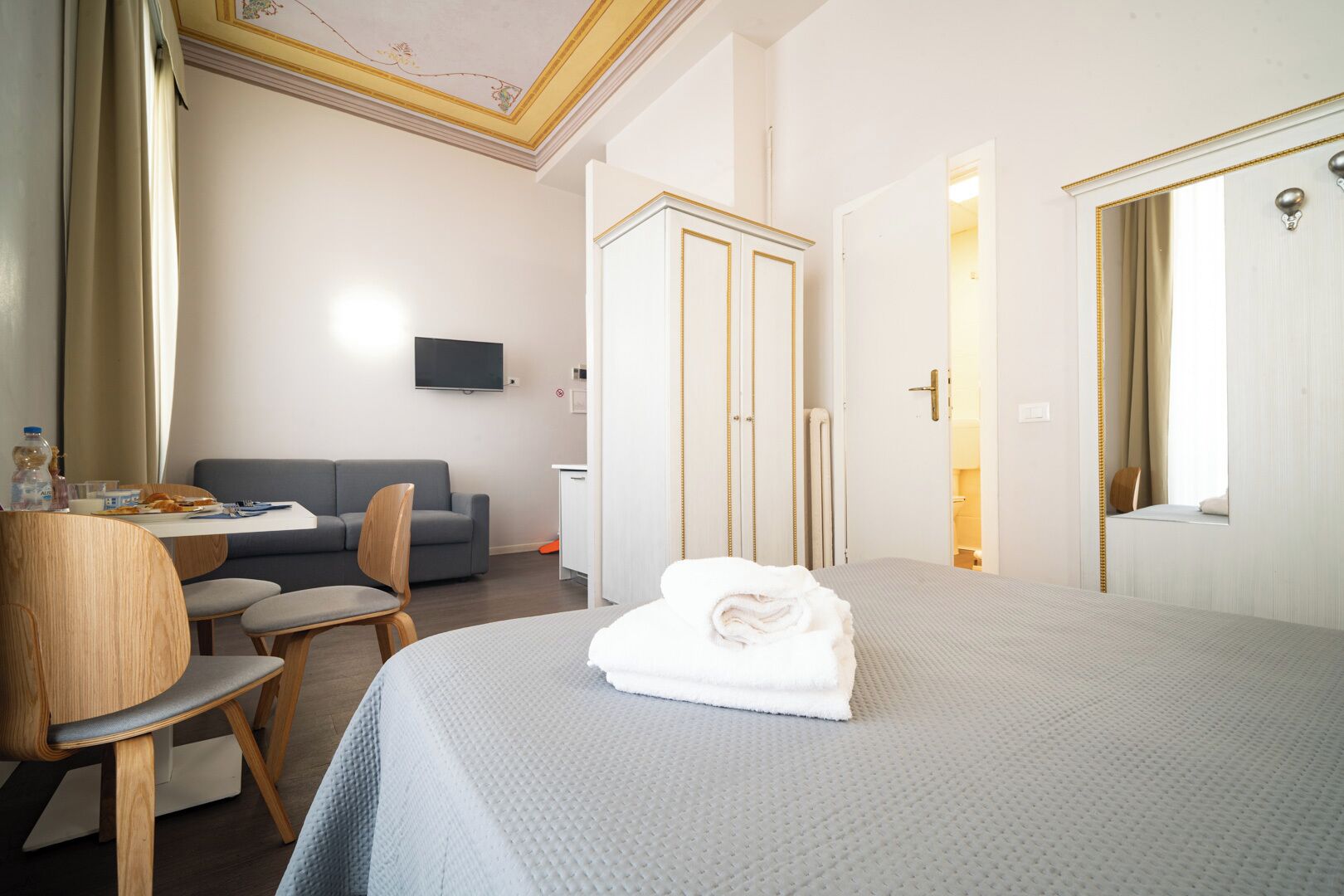 Quarto de hotel com cama, secretária com cadeira, sofá, guarda-roupa e televisão.