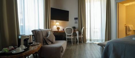 A hotel room with a bed, a desk with a lamp, a chair, a small table with a coffee maker, and curtains.