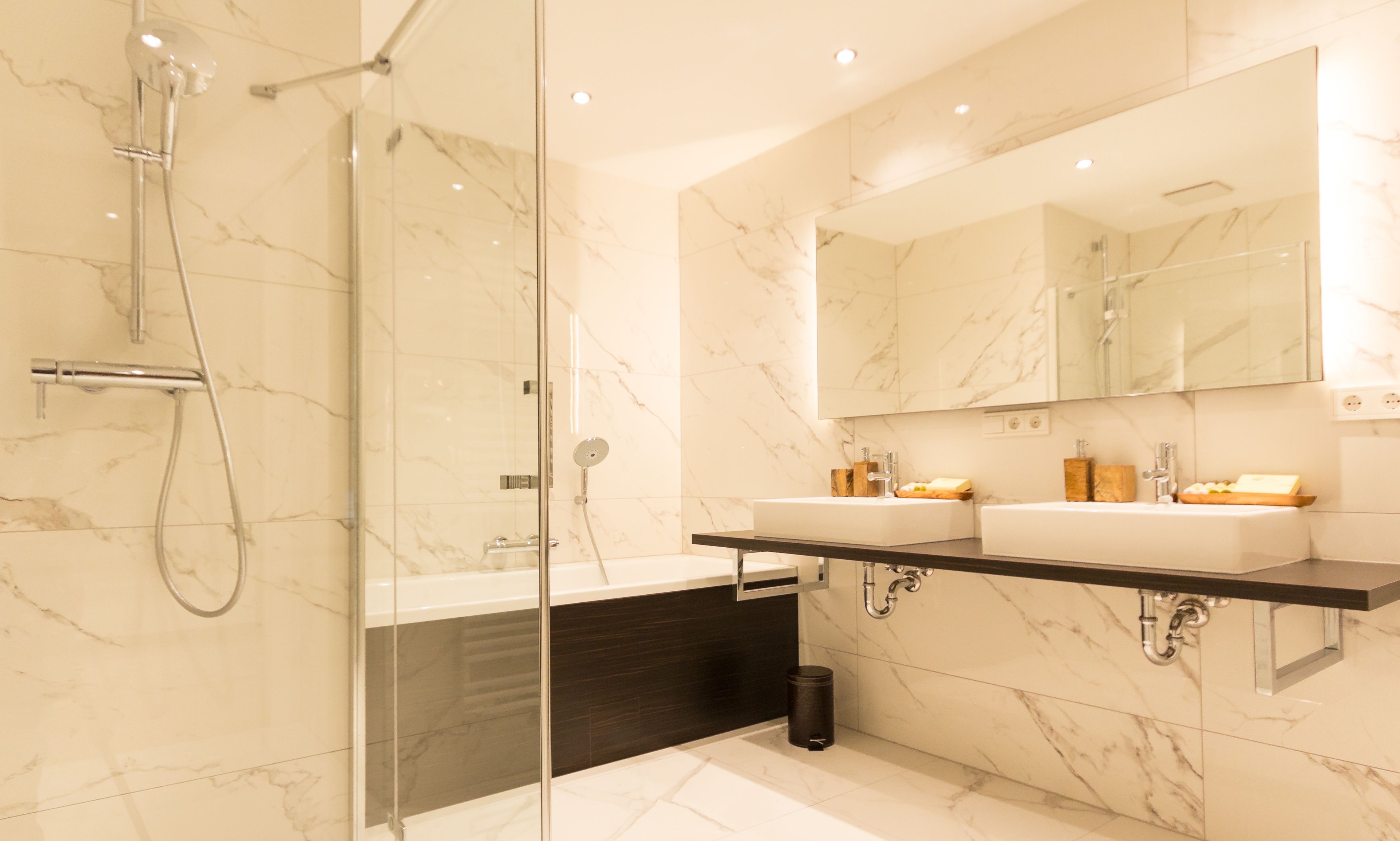 Un baño moderno con ducha de vidrio, dos lavamanos y un espejo grande.